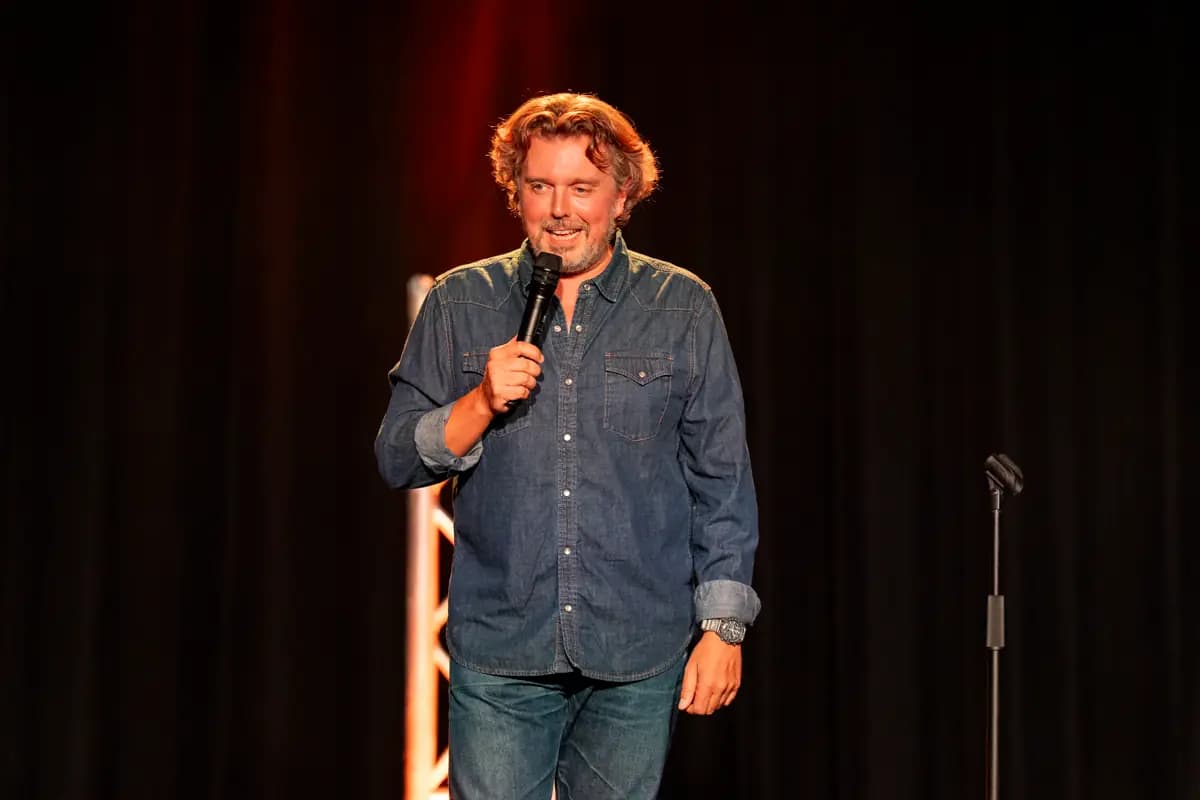 Un humoriste en chemise en jean, micro en main, sous les projecteurs