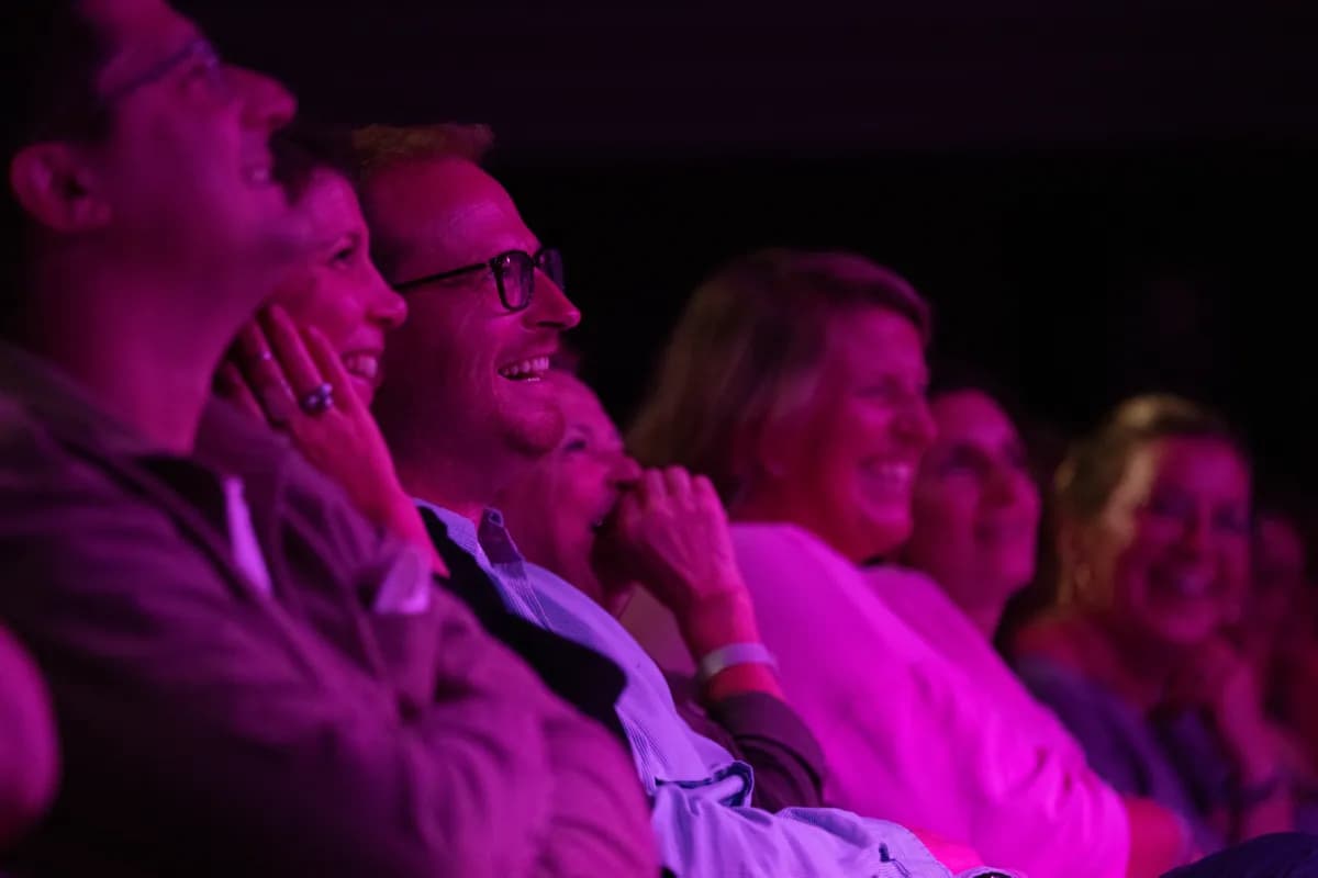Des spectateurs rient dans la salle, baignés de lumière rose