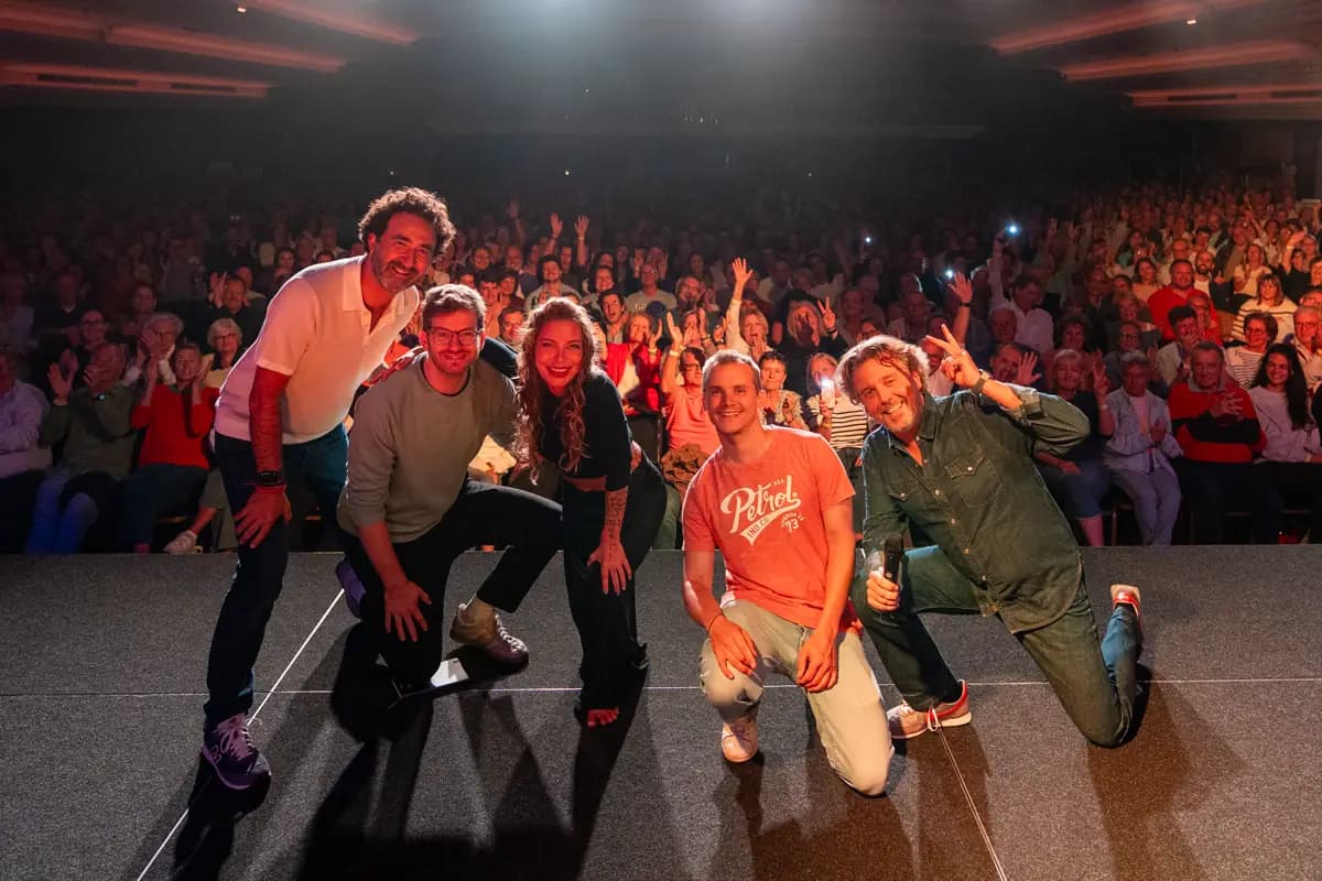 Les humoristes posent sur scène devant une salle comble qui lève les bras
